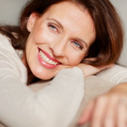 Eine Frau liegt mit ihrem oberkörper auf der Lehne des Sofas und legt ihren Kopf auf ihrer Hand ab